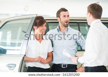 Happy couple in car salon with car salesman