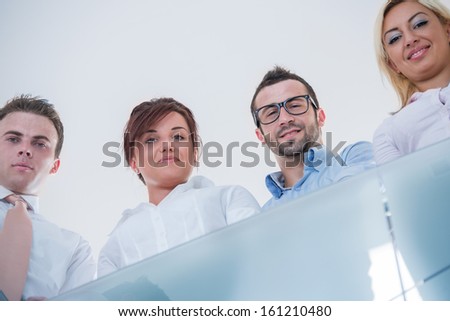 Four posing business people behind a modern glass railing