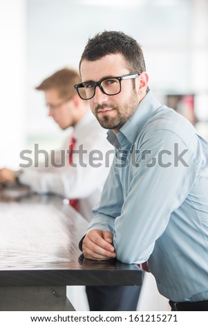 Business man posing leaning on a high table in company environment