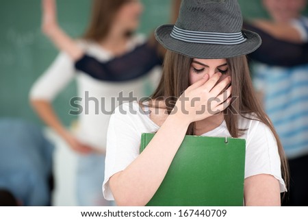 Sad female student with hat holding books in classroom