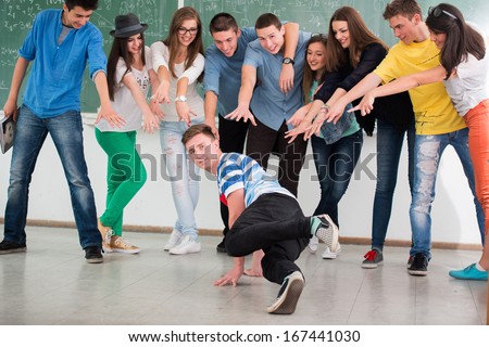 Student break dancing in classroom surrounded by classmates