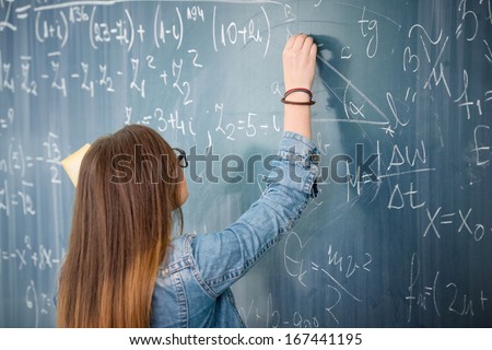 Schoolgirl With Glasses Solving Math Problem On Blackboard