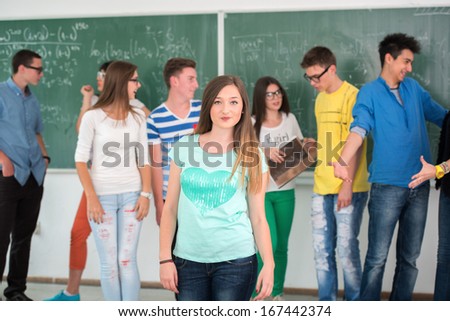 Cute schoolgirl standing in classroom in front of blackboard