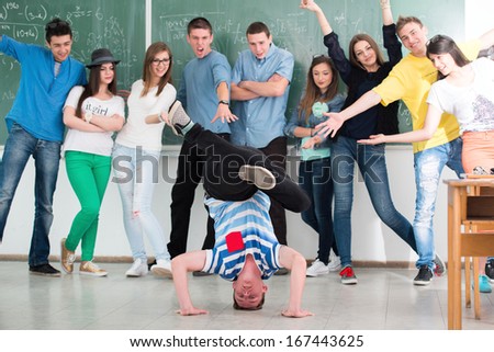 Happy high school student posing in classroom with his friends in background