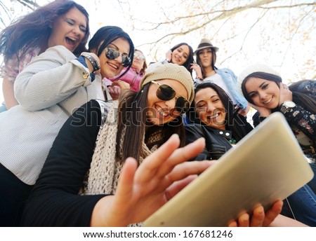 Happy teen girls having good fun time outdoors using tablet for reading in park