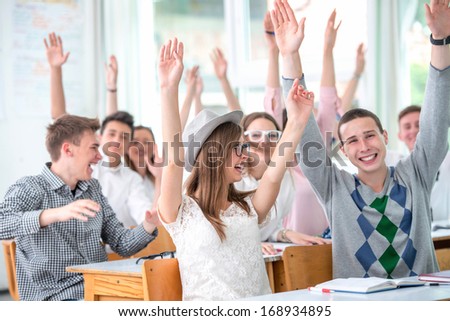 Smiling highschool students in classroom holding hands in the air