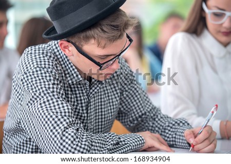 Teenage student with hat writing in classroom