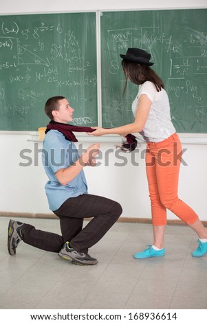 Boy kneeling in front of girl in classroom in front of blackboard
