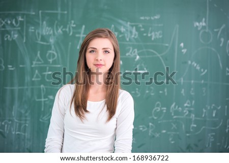 Sweet schoolgirl posing in front of chalkboard in classroom