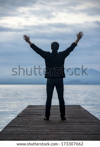 Man standing on pier with his hands lifted in the air