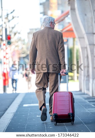 Old man walking with suitcase pulling behind