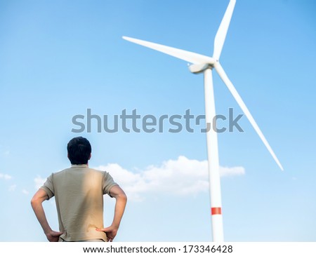 Man from behind looking a wind turbine from ground