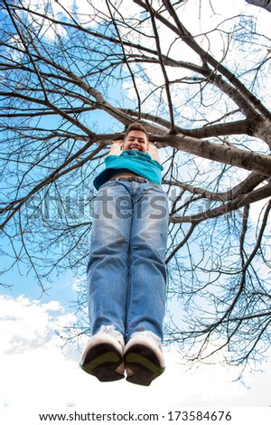 Happy smiling teenager climbing on a tree in park