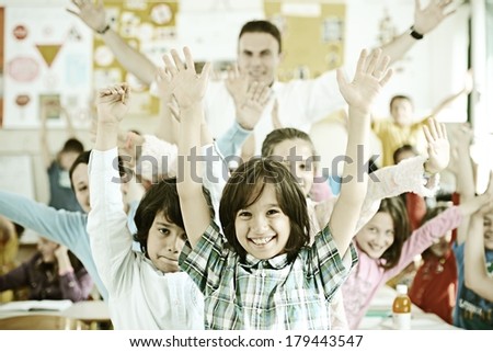 Cheerful kids at school room having fun activity with teacher rising hands up