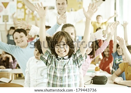 Cheerful kids at school room having fun activity with teacher rising hands up