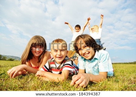 Happy boys and girls sitting on summer grass meadow