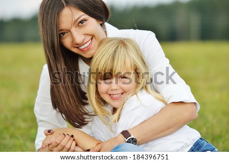 Mother and her little girl on green summer grass meadow having fun