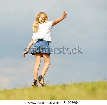Happy little blonde girl on summer grass meadow in nature having happy time and jumping