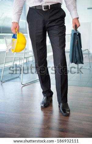 Legs of business man holding hard hat and briefcase in office