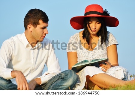 Young couple enjoying love on summer meadow reading book