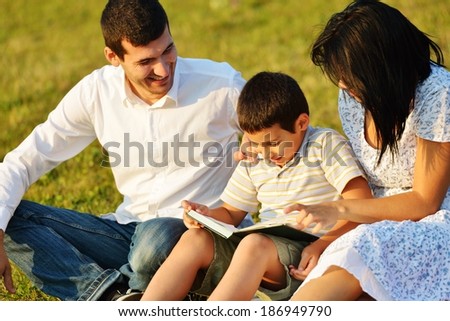 Cheerful family on beautiful summer meadow enjoying learning from the book