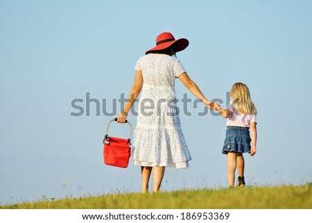 Mother and daughter walking together on beautiful summer meadow enjoying and having fun
