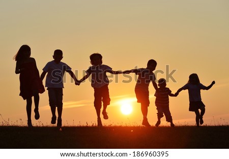 Happy children silhouettes on summer meadow running and jumping