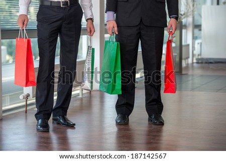 Legs of two men holding paper bags in modern environment
