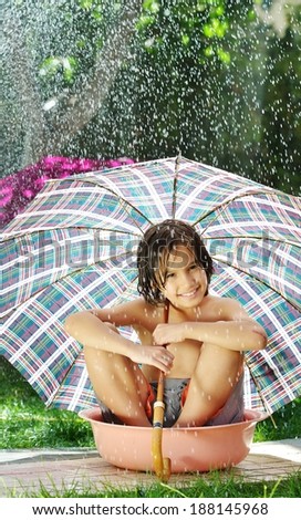 Kids playing with sprinkler water holding umbrella on summer backyard