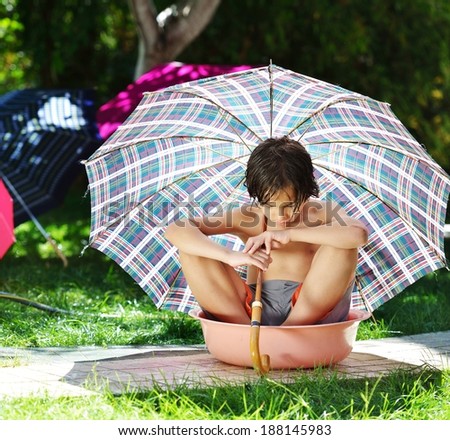 Kids playing with sprinkler water holding umbrella on summer backyard