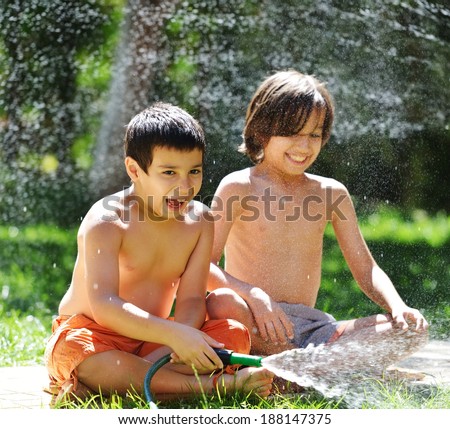 Happy kids playing and splashing with water sprinkler on summer grass yard