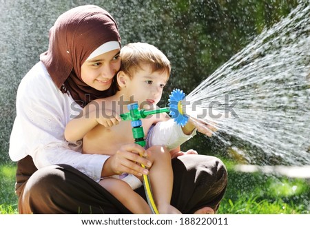 Beautiful Middle Eastern Arabic girl having baby playing with water sprinkler in garden
