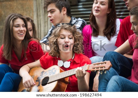 Happy teenage girl with guitar playing with a group of friends