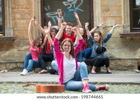 Teenage girl holding hands in the air sitting on the street in front of her waving friends