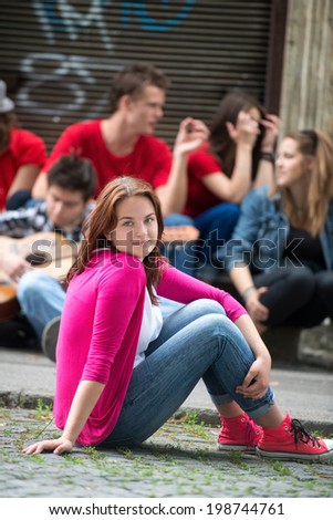Handsome young girl posing sitting on the street in front of group of teenagers