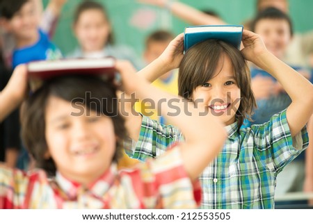 Group of kids with books on heads smiling in classroom