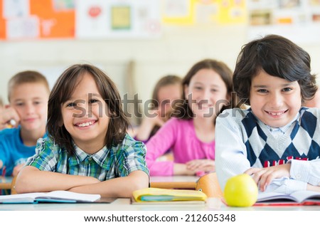 Cheerful kids sitting with apple on desk in classroom