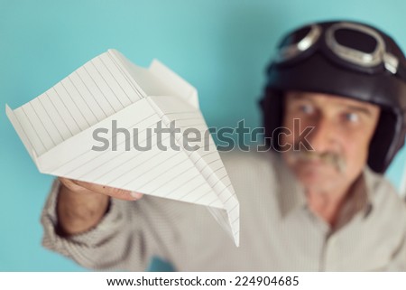 Senior funny man as a pilot with hat and glasses using paper plane