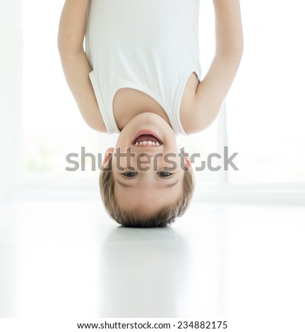 Portrait of happy baby boy playing upside down indoors in living room on white floor walking on hands