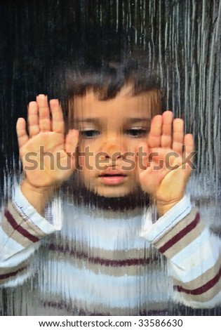 A little sad kid looking through glass