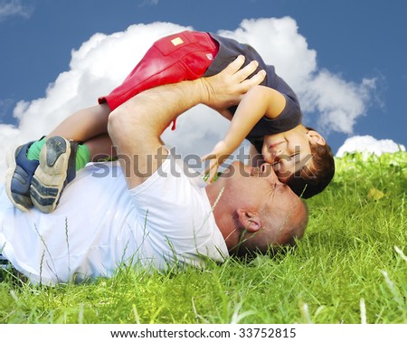 A parent and his kid laying and smiling on grass