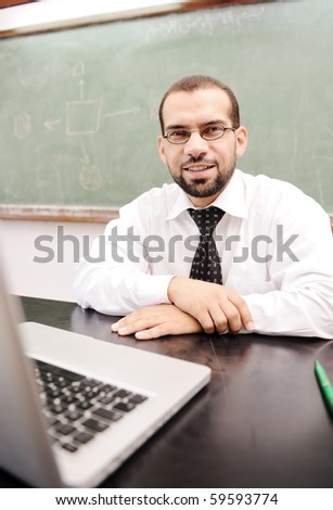 Happy positive teacher with laptop on desk in classroom