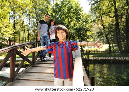 Beautiful scene of young happy family in natural park, three members: mother father behind and son in front looking at camera