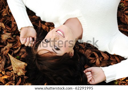 Young beauty girl laying on autumn ground and leaves, perfect face and natural skin