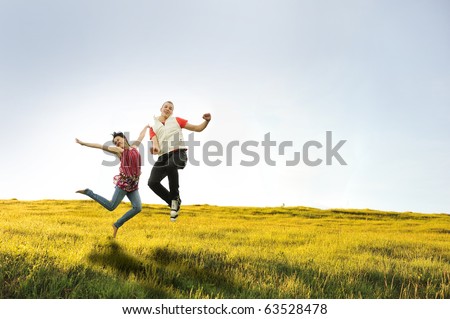 Happy teenager couple, friends or boyfriend and girlfriend, jumping on beautiful green meadow in nature