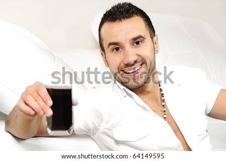 Young happy man drinking juice, sitting in room and smiling