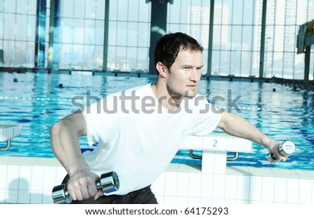 Young sporty man doing exercises with light weights in gym beside the pool