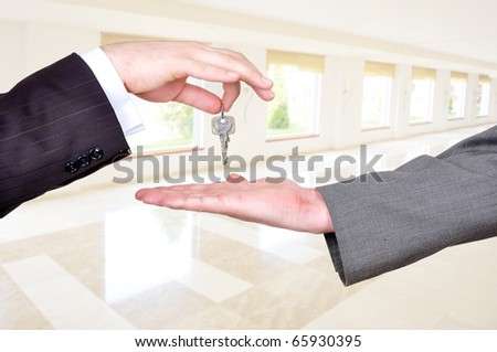 Hands exchanging the key to success, selling and buying an estate, white big modern building indoor in background, business and home concept