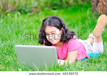 happy children in nature outdoor, little girl working and playing on laptop, laying on green meadow