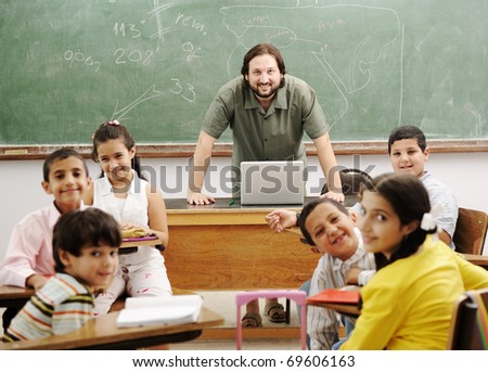 Teacher with children in classroom using laptop, boys and girls in school together learning